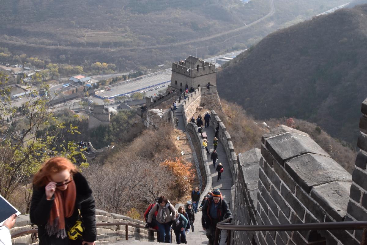 Visitors climb a steep stretch of the Great Wall, a watchtower and valley parking area far below