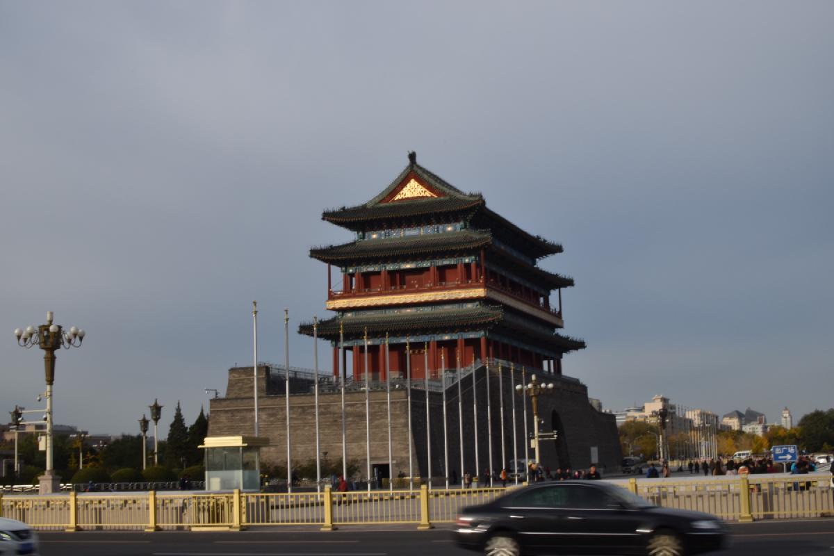 The Zhengyangmen gate tower rises over a Beijing boulevard as a car passes gold-colored railings