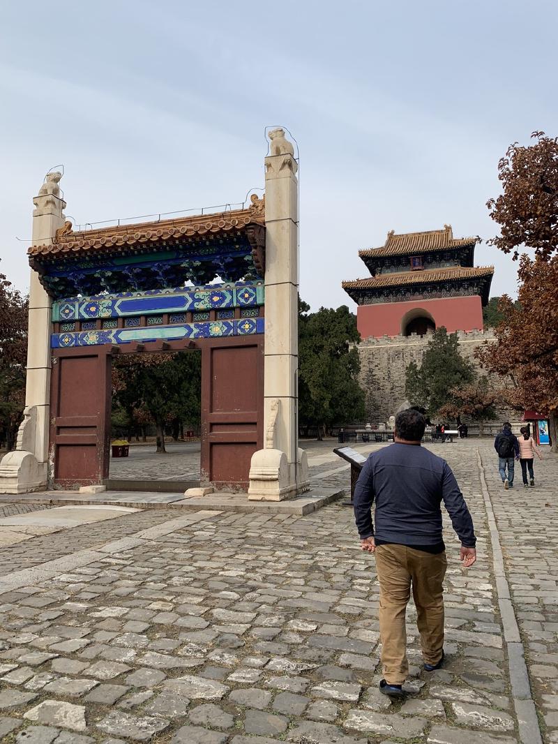 Man walks a cobbled path past a painted gateway toward the red Soul Tower at the Ming Tombs