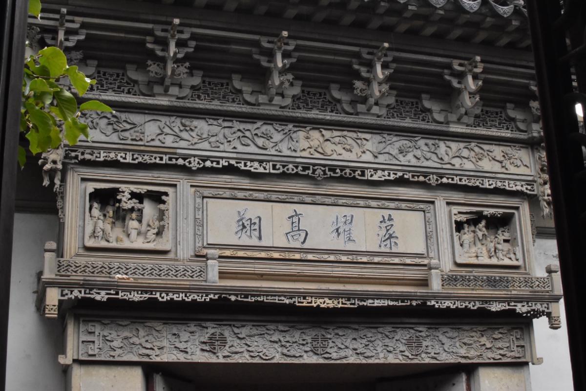An ornate carved grey stone gateway with a Chinese inscribed plaque and figure reliefs, Shanghai, China