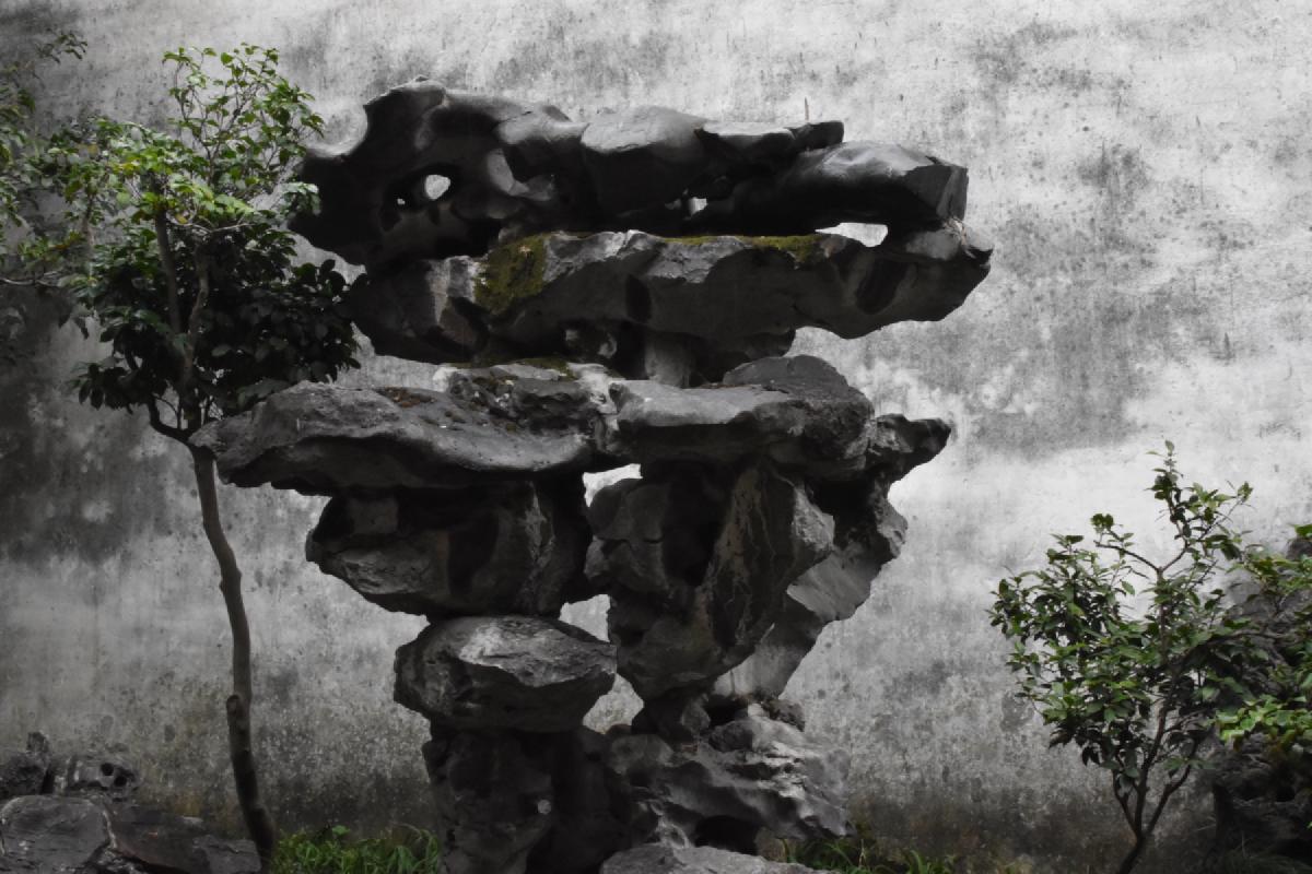 A stacked scholar&rsquo;s rock full of holes and mossy ledges stands against a weather-stained white garden wall in Shanghai