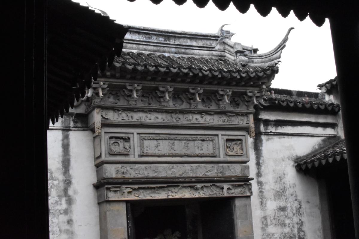 Carved grey stone gateway with an inscribed plaque and upswept tiled roof, seen from a dark courtyard in China