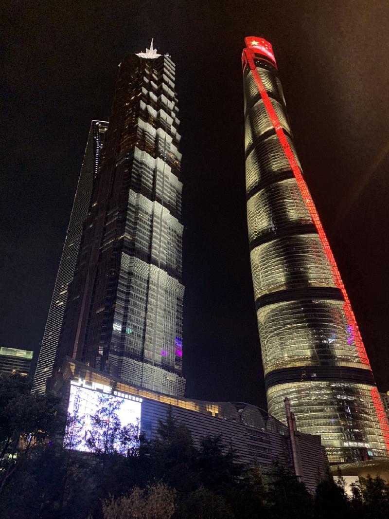 Looking up at night at the Jin Mao Tower and the twisting Shanghai Tower lit red along its edge