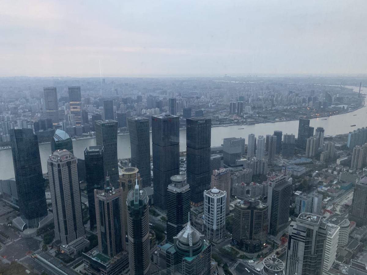 Hazy daytime view over Shanghai from a high window, office towers crowding a bend in the Huangpu River